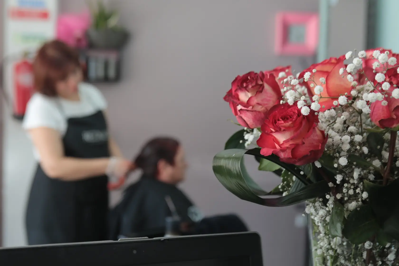 A Patrícia a cortar o cabelo de uma cliente, com rosas em primeiro plano no balcão do salão